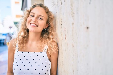 Fototapeta premium Young beautiful caucasian woman with blond hair smiling happy outdoors on a summer day leaning on the wall