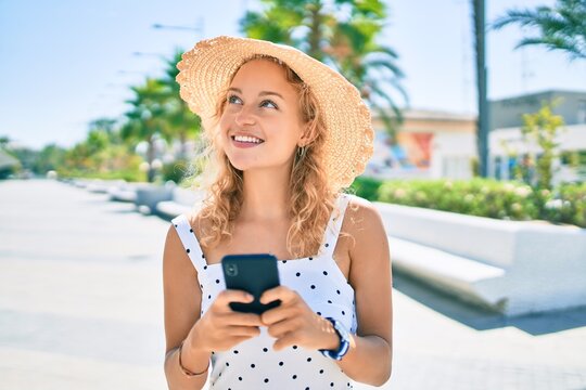 Young beautiful caucasian woman with blond hair smiling happy outdoors using smartphone