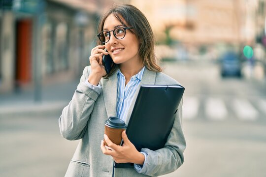 Young hispanic businesswoman talking on the smartphone and drinking take away coffee at the city.