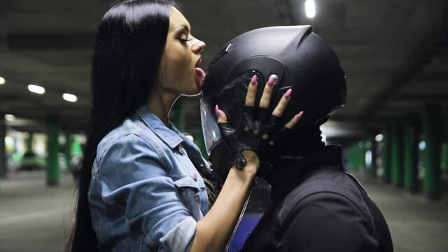 Young brunette girl licks the black helmet of a motorcyclist with her tongue at night