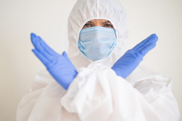 Fototapeta premium Female doctor in a protective suit shows a stop with crossed arms. Stop the coronavirus