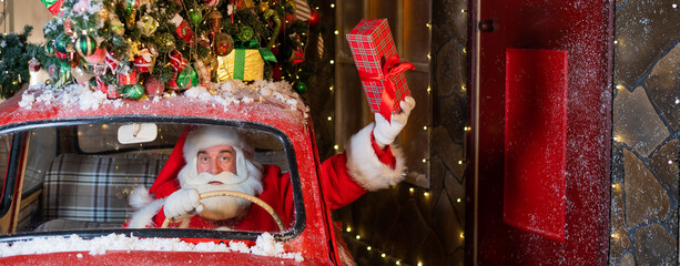 Santa Claus delivers presents behind the wheel of a red car and waves a gift box out of the window