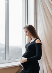 A pregnant girl is breathing fresh air from the window