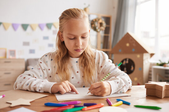 Front View Portrait Of Blonde Teenage Girl Drawing Or Doing Homework While Sitting At Desk In Home Interior, Copy Space