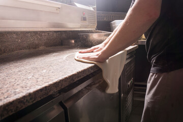 The pizza maker rolls out the dough. The chef prepares the pizza base
