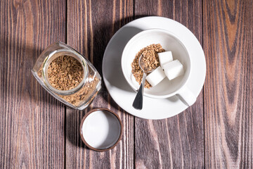freeze-dried coffee, a Cup with freeze-dried coffee poured into it and a piece of refined sugar at the bottom of the Cup, a jar with an open lid on a wooden table