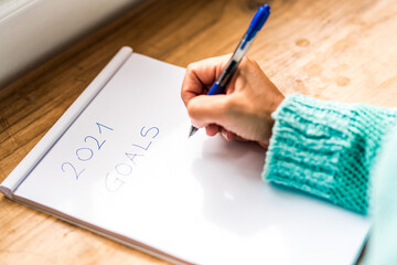close up of hand of a woman wearing blue shirt or sweater writing in a paper sheet her 2021 goals with a pen