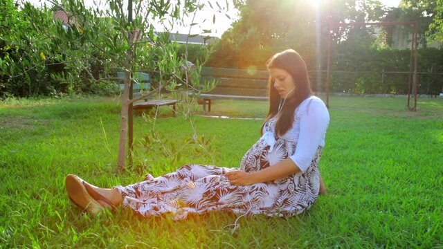 Happy pregnant woman listening music in garden
