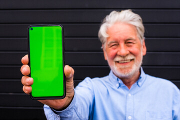 one old and mature senior man holding a mobile phone with green screen and showing it to the camera