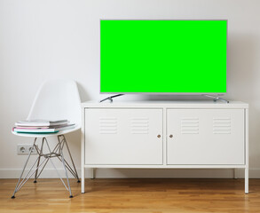 Widescreen modern green screen TV for text and video on a chrome stand against a white wall.