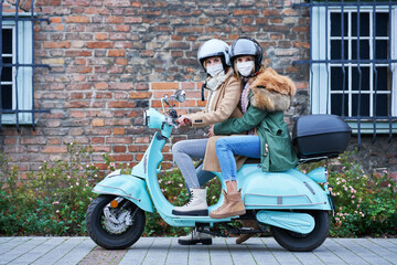 Two women wearing masks and commuting on scooter