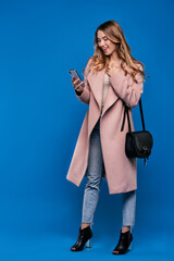 .Young beautiful blonde girl in a raincoat on a blue background with mobile phone