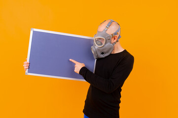 Funny strange man in respirator posing with a board  over orange background