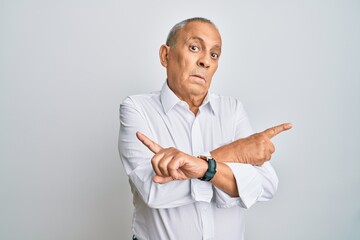 Handsome senior man wearing casual white shirt pointing to both sides with fingers, different direction disagree