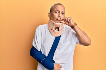 Handsome mature senior man wearing cervical collar and arm on sling mouth and lips shut as zip with...