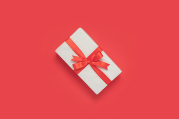 White gift with a bow ribbon on red background with copy space. Christmas and New Year holidays concept.