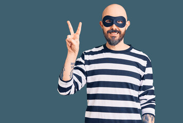 Naklejka premium Young handsome man wearing burglar mask showing and pointing up with fingers number two while smiling confident and happy.