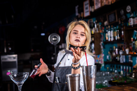 Charismatic girl mixologist demonstrates the process of making a cocktail