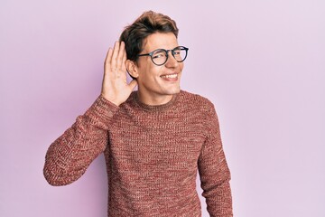 Handsome caucasian man wearing casual sweater and glasses smiling with hand over ear listening an hearing to rumor or gossip. deafness concept.