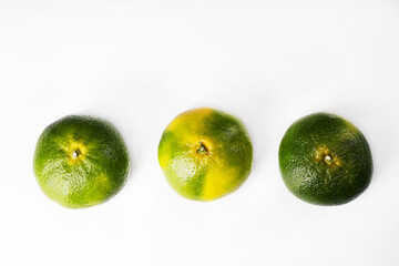 Three green tangerines on a white background. The color of tangerines is yellow and green. New Year's fruit. Unripe tangerine. Fruit for the Christmas holidays.