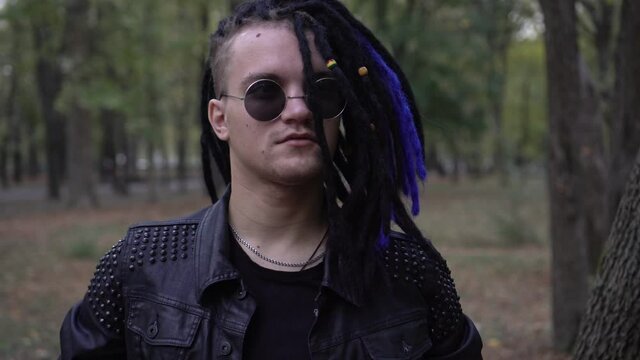 Portrait of a stylish man in a black leather jacket, round glasses and hair with dreadlocks