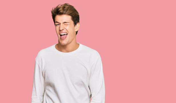 Handsome caucasian man wearing casual white sweater winking looking at the camera with sexy expression, cheerful and happy face.