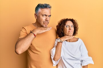 Beautiful middle age couple together wearing casual clothes cutting throat with hand as knife, threaten aggression with furious violence