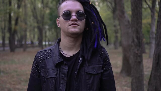 Stylish man in black leather jacket, round glasses and dreadlocks hair outdoors