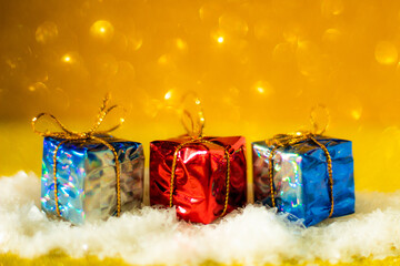 Simple Christmas concept: small, decorative gifts in the snow, golden glitter background, selective focus, free copy space 