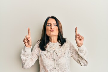 Middle age brunette woman pointing up with fingers looking at the camera blowing a kiss being lovely and sexy. love expression.