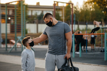 A father and child stand on a sports field in masks after training during sunset