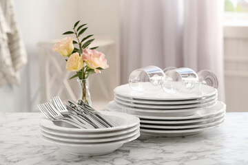 Fototapeta na wymiar Set with clean dishes and vase of flowers on white marble table