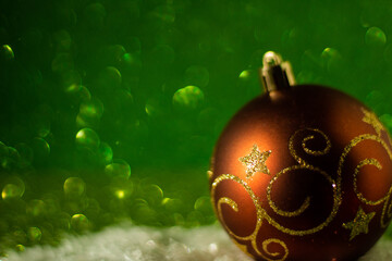 Perfect and simple Christmas concept: decorative Christmas ball with golden glitter, green glitter background, selective focus, free copy space