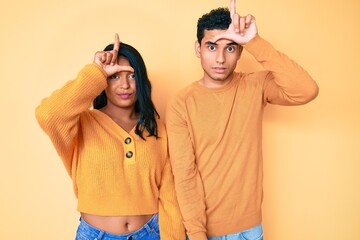 Beautiful latin young couple wearing casual clothes together making fun of people with fingers on...