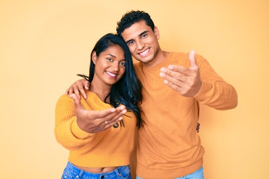 Beautiful latin young couple wearing casual clothes together smiling friendly offering handshake as greeting and welcoming. successful business.