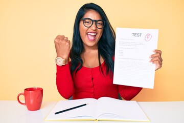 Beautiful latin young woman with long hair showing a failed exam screaming proud, celebrating victory and success very excited with raised arms