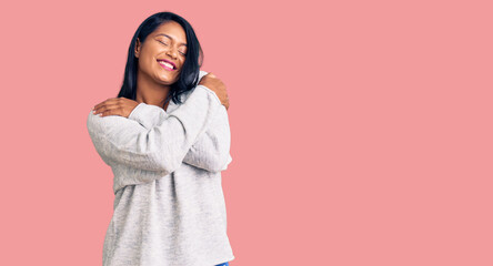 Hispanic woman with long hair wearing casual clothes hugging oneself happy and positive, smiling confident. self love and self care