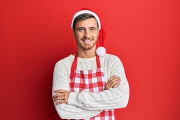 Handsome caucasian man wearing baker apron and christmas hat happy face smiling with crossed arms...