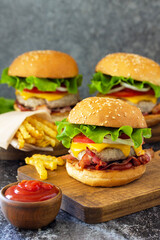 Homemade burgers with cutlet beef, cheese, bacon, french fries and ketchup on a slate table. Copy space.