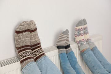 Family warming legs on heating radiator near white wall, closeup