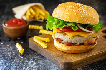 Homemade burgers with cutlet beef, cheese, bacon, french fries and ketchup on a slate table.