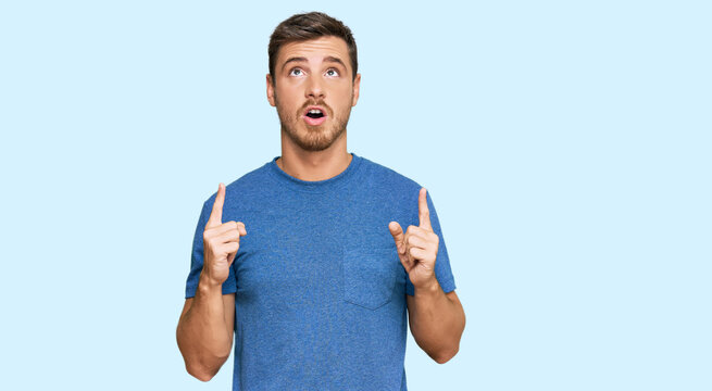 Handsome caucasian man wearing casual clothes amazed and surprised looking up and pointing with fingers and raised arms.