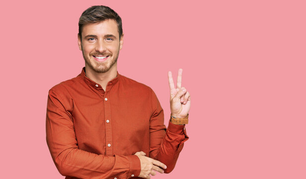 Handsome caucasian man wearing casual clothes smiling with happy face winking at the camera doing victory sign. number two.