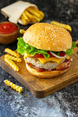 Delicious burgers with cutlet beef, bacon, french fries and ketchup on a slate table.