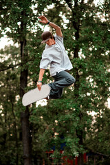 guy in cap and with skateboard simulator jumping up against the backdrop of green trees