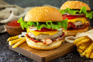 Delicious burgers with cutlet beef, bacon, french fries and ketchup on a slate table.