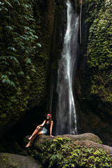 Beautiful girl at a waterfall on the island of Bali Indonesia, vertical view. Sexy woman at the waterfall. Young and beautiful woman at the waterfall. Beautiful woman posing at a waterfall.