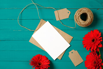 Envelope, blank paper card and flowers on green background