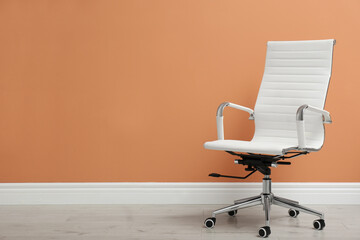 Modern office chair near orange coral wall indoors. Space for text