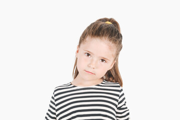 Serious girl looking at camera with head tilted to one side. Posing little girl wearing striped shirt. Girl listening with attention.